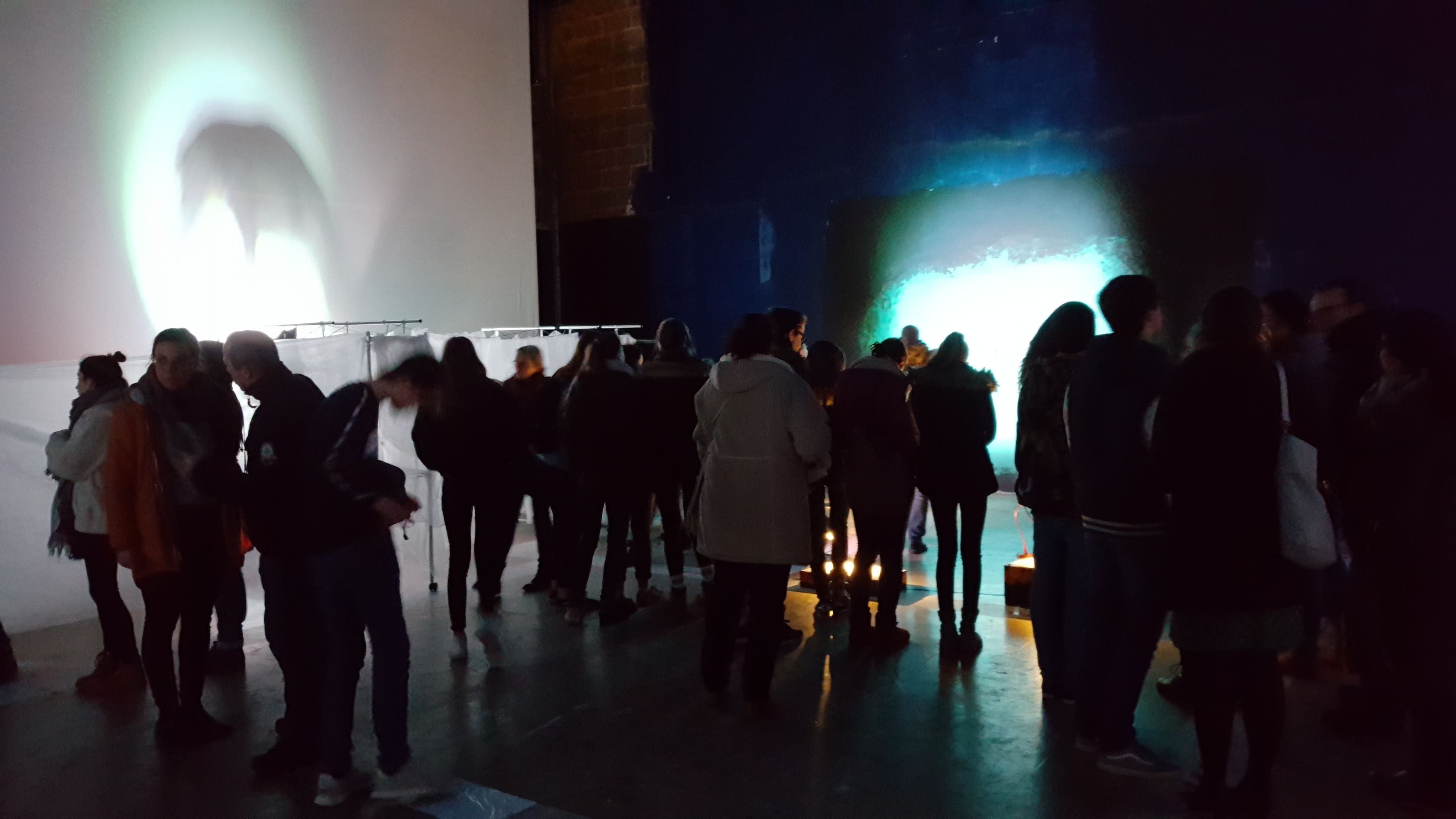 Eine Ausstellungssituation mit vielen Menschen in einem dunklen Raum und Beleuchtung