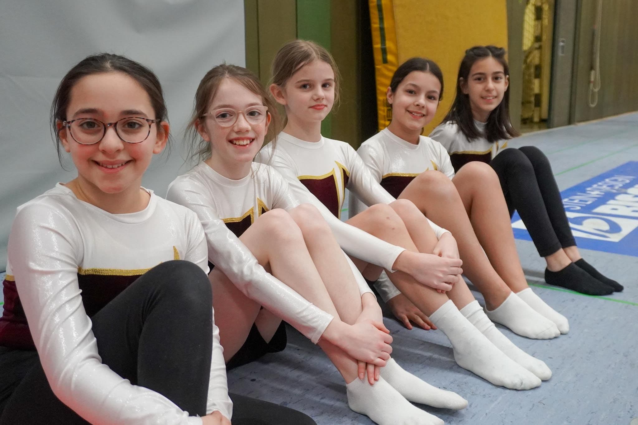 Turnerinnen sitzen in einer Sporthalle auf dem Hallenboden.