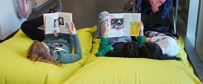 three girls are laying on bean bags reading books .