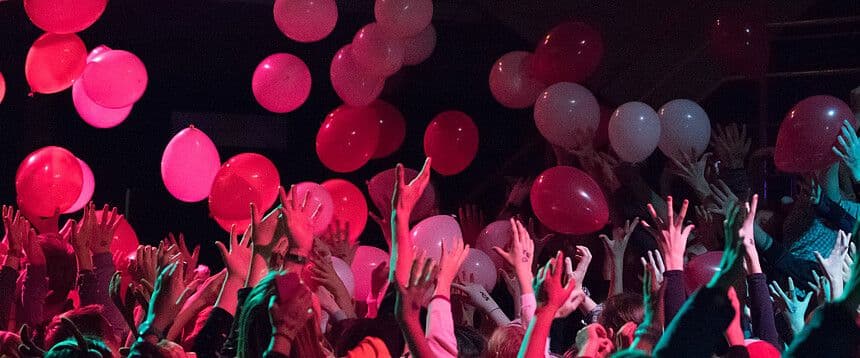 a crowd of people are holding balloons in the air at a party .