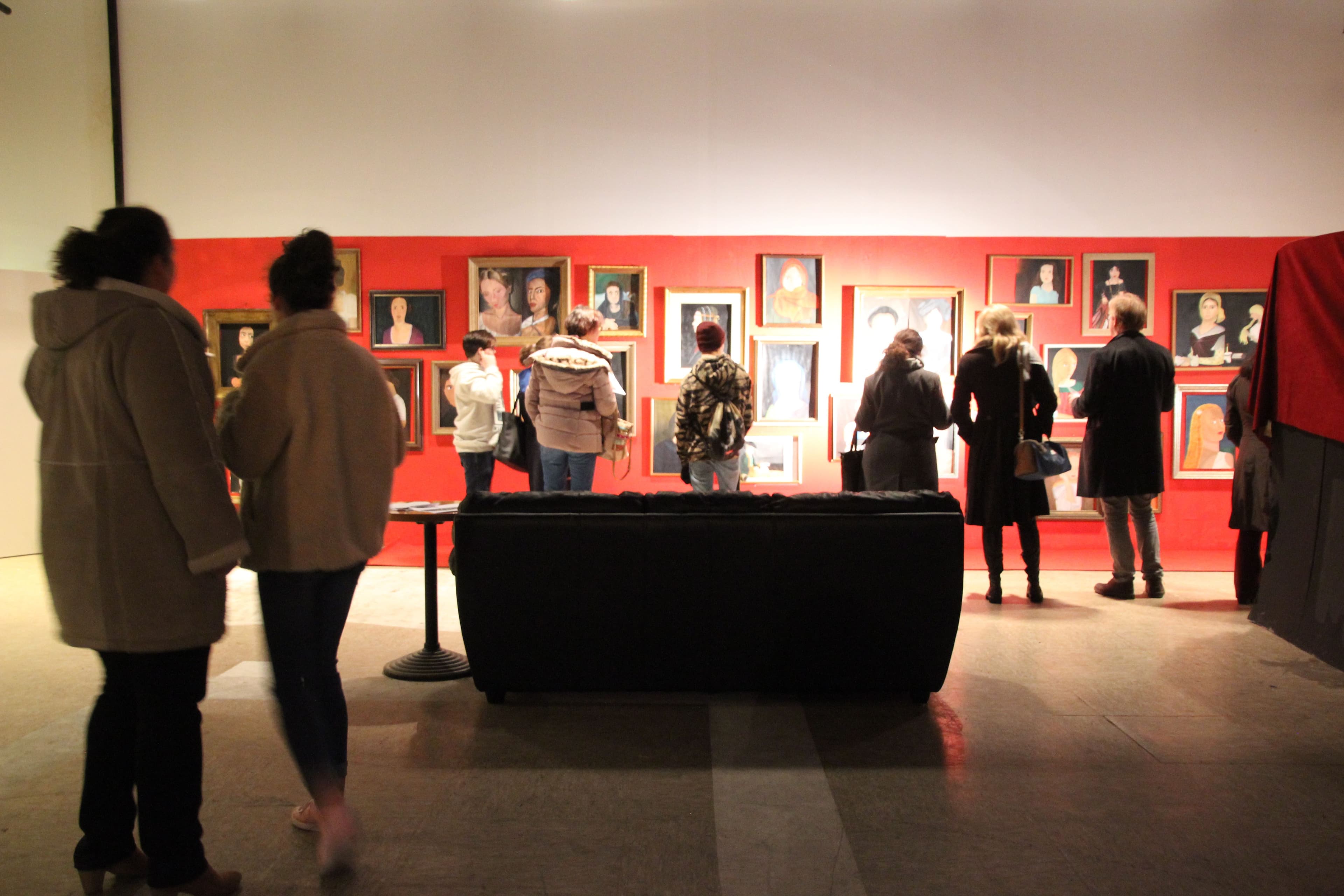 a group of people are looking at paintings on a wall in a museum .
