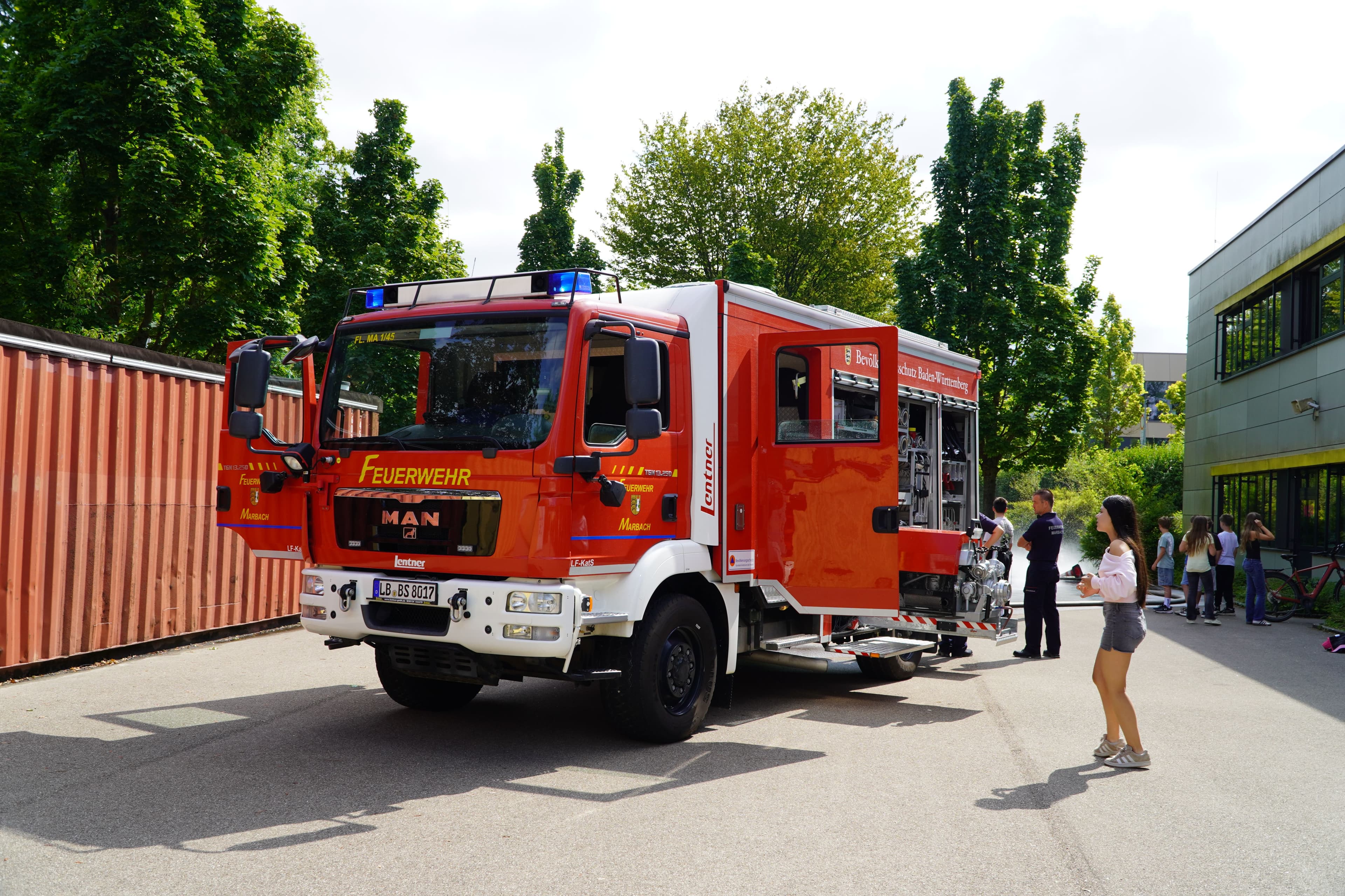 A red fire truck with open doors and compartments, surrounded by people at an outdoor event.