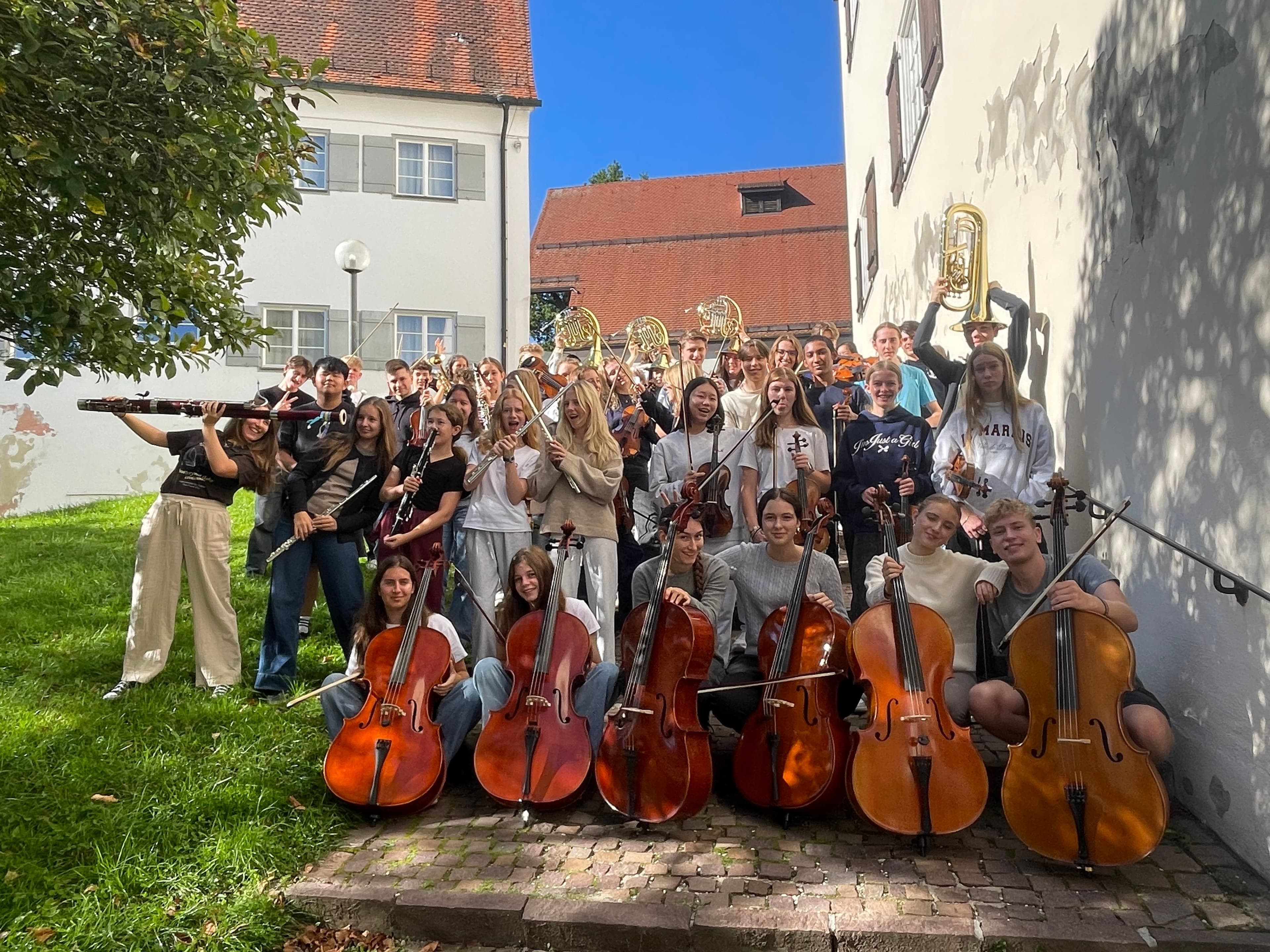 Eine Gruppe Menschen mit Instrumenten steht an einer Hauswand im Freien