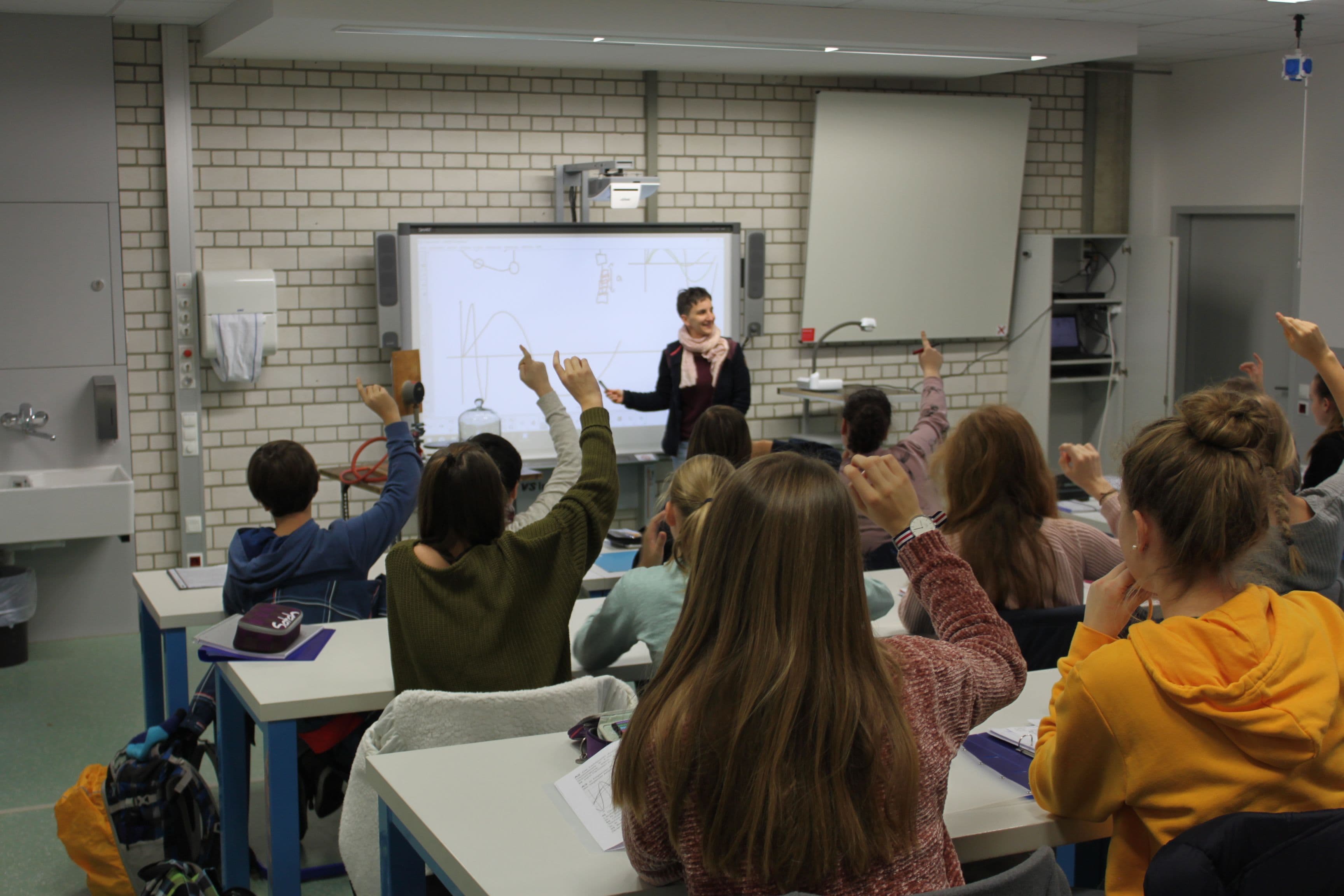 a group of students are raising their hands in a classroom to answer a question .
