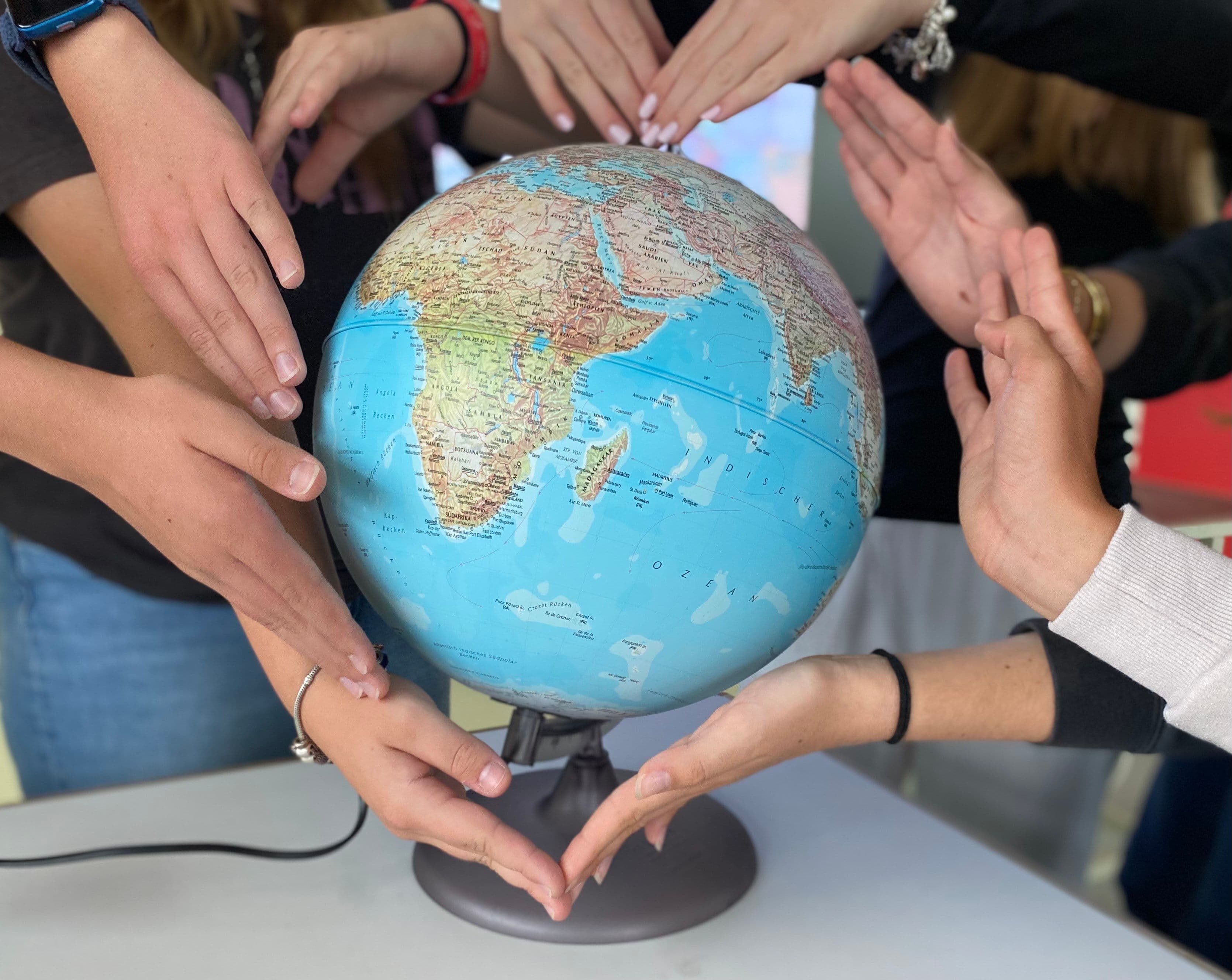 eine Gruppe von Menschen hält Hände um einen Globus