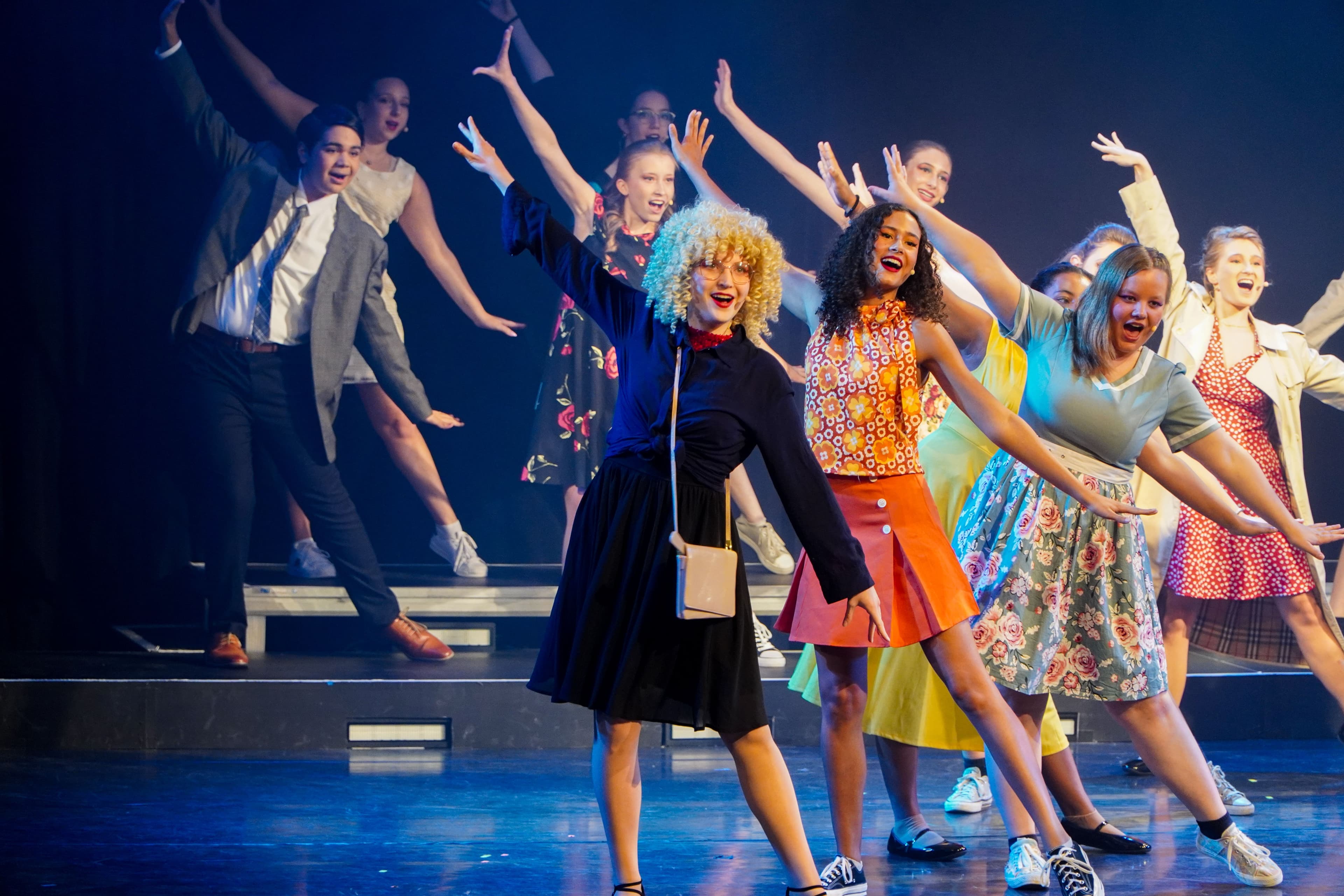 Schüler in Kostümen der 60er in Tanzpose auf einer Bühne.