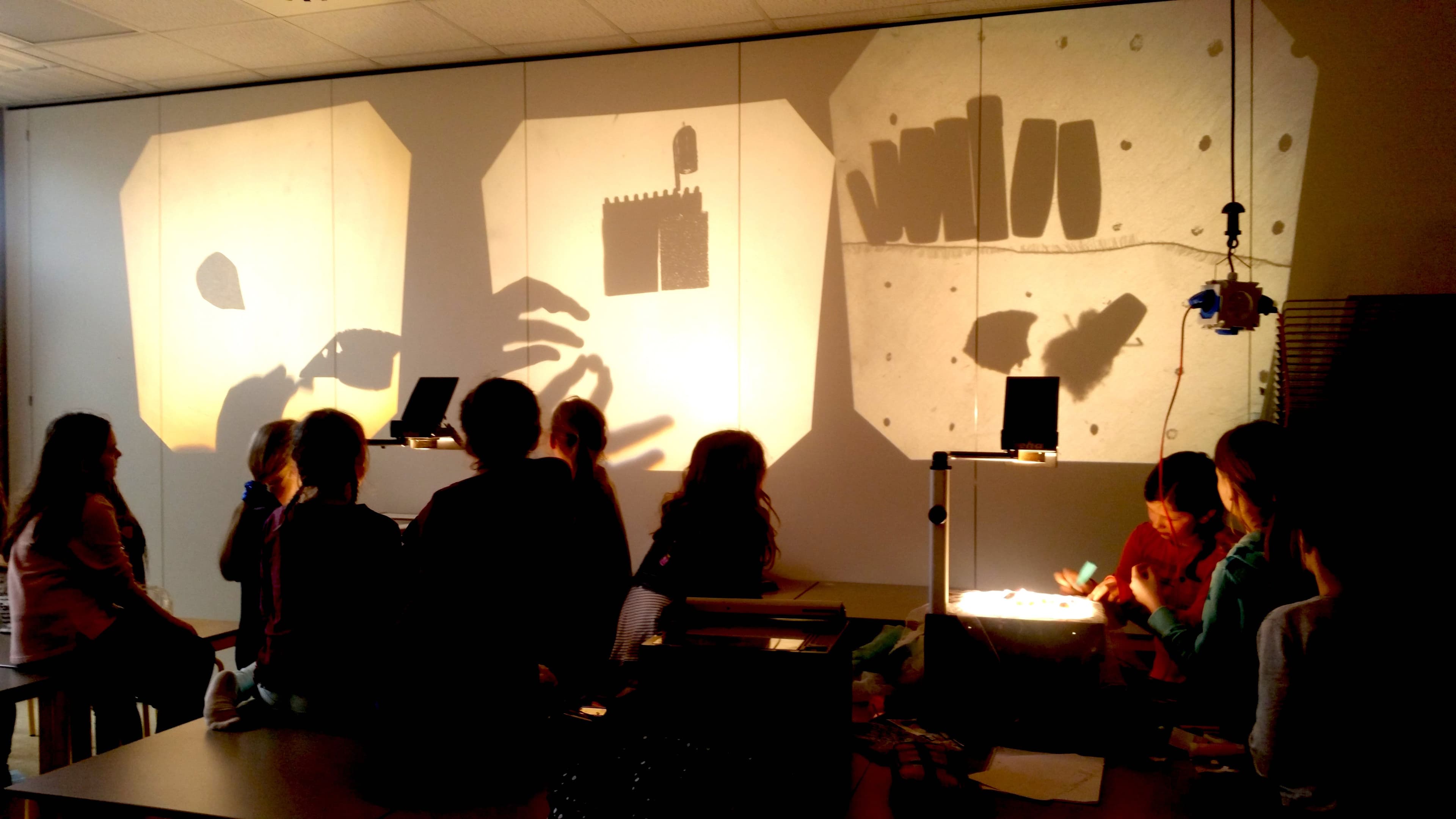 a group of people are sitting at a table in front of a wall with shadows projected on it .