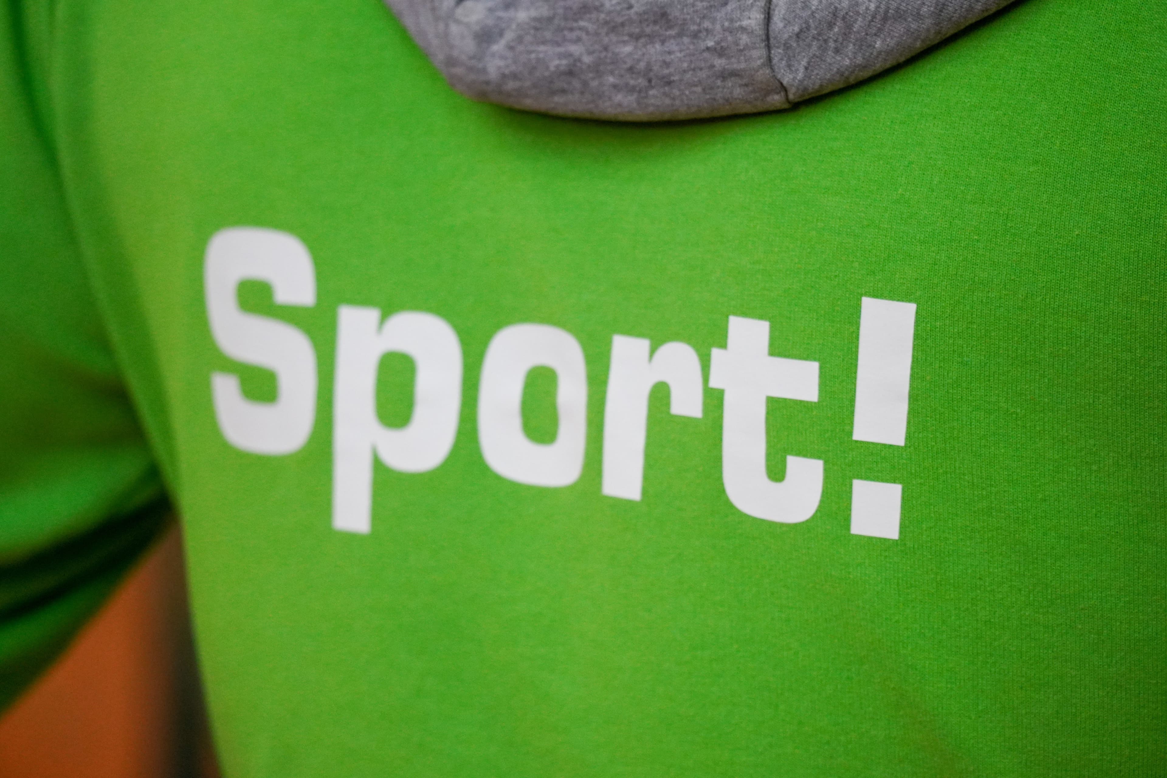 Schriftzug "Sport" auf einem grünen Pullover.