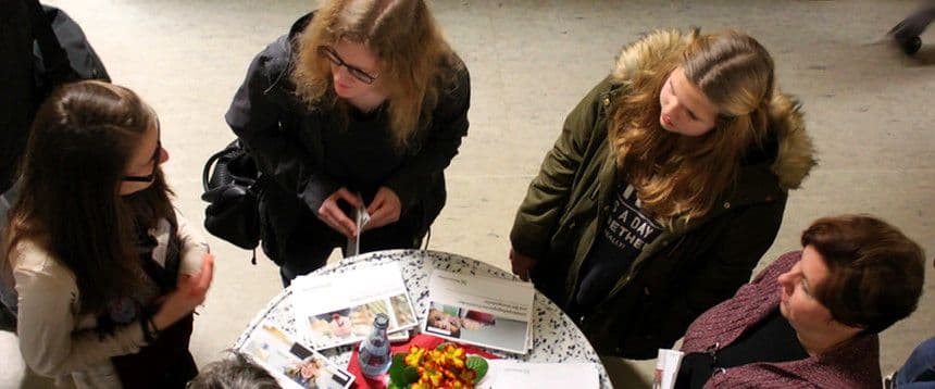 Menschen stehen um einen runden Stehtisch und unterhalten sich