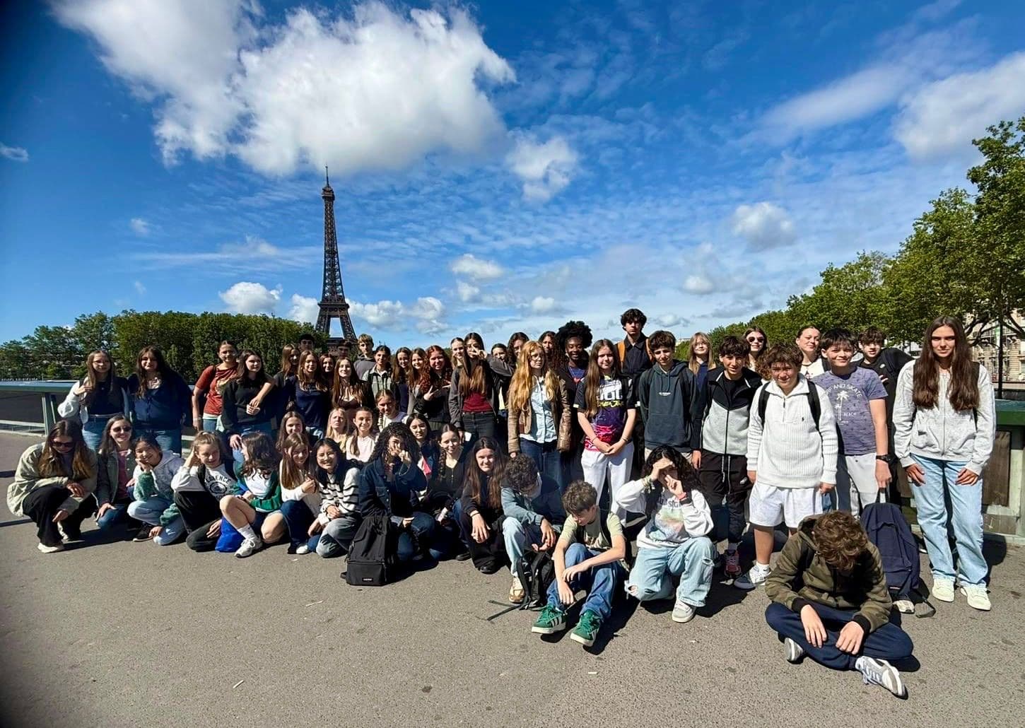 A large group of young people poses outdoors with the Eiffel Tower in the background.